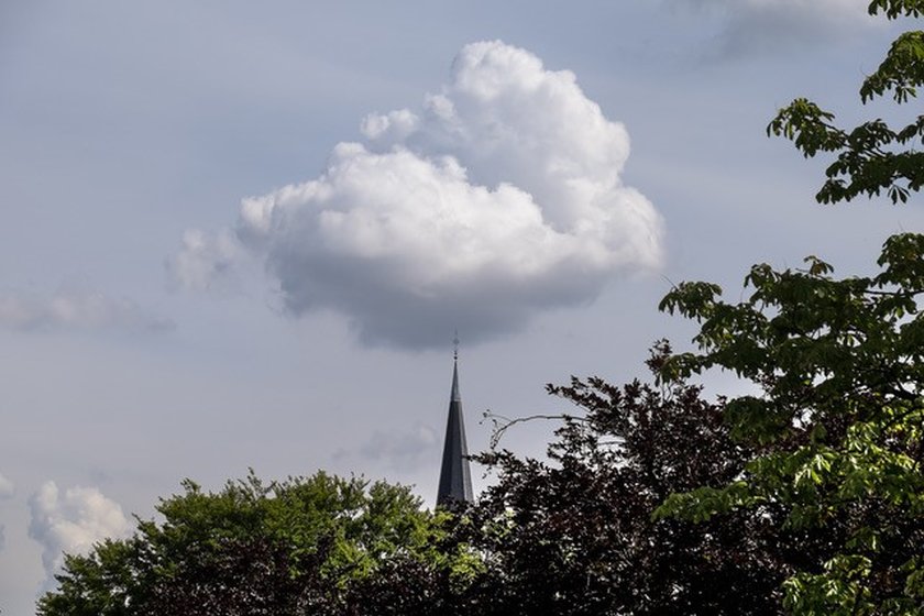 die Spitze eines Kirchturms berührt eine Wolke
